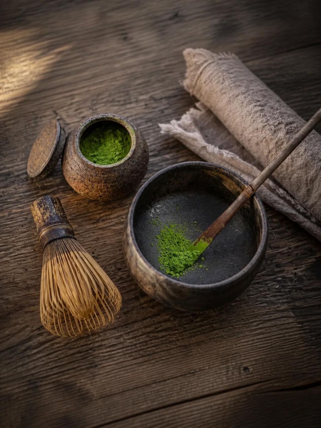 Ceremonial matcha powder and bamboo whisk resting in a rustic dark bowl